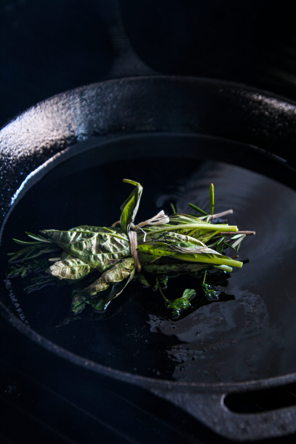 Herb bundle and olive oil in cast iron pan